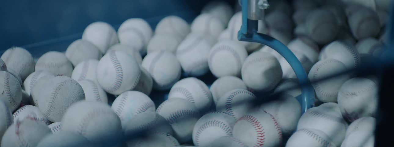 Blue arm stirs white baseballs in bin