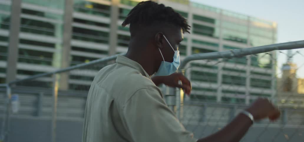 A man wearing a medical mask stands beside a wire fence trying to look over it