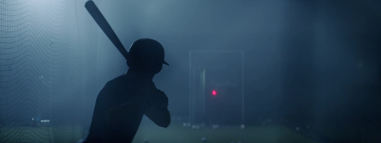 A baseball player swings and hits a ball thrown to him by a pitching machine