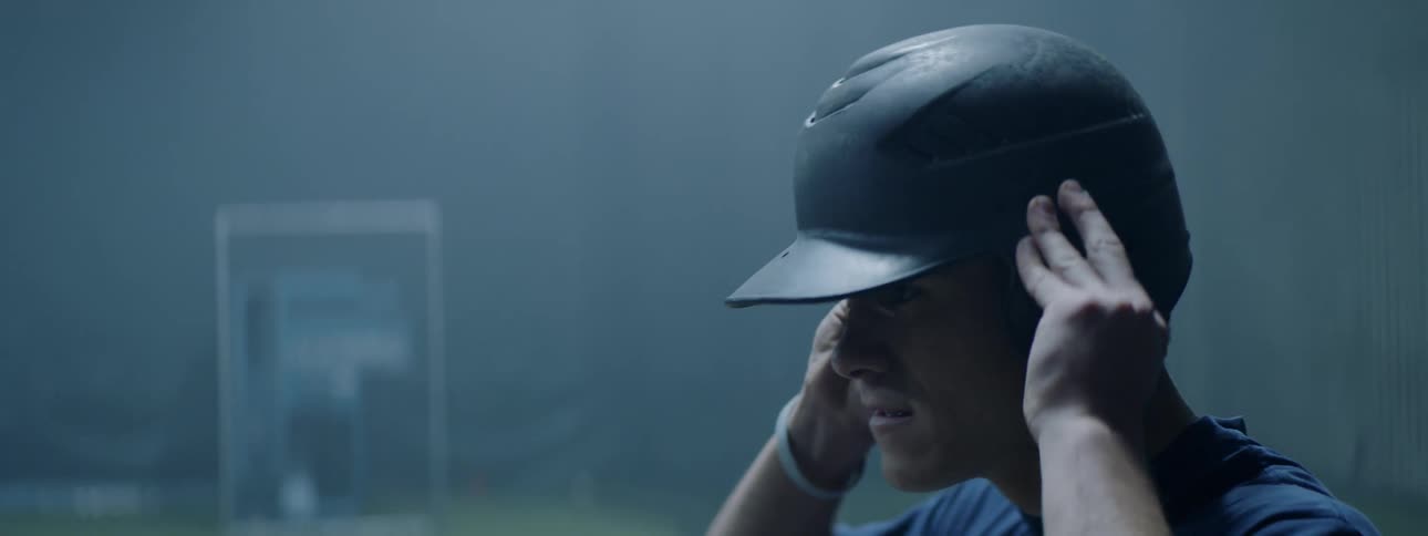 A baseball player is putting on a helmet