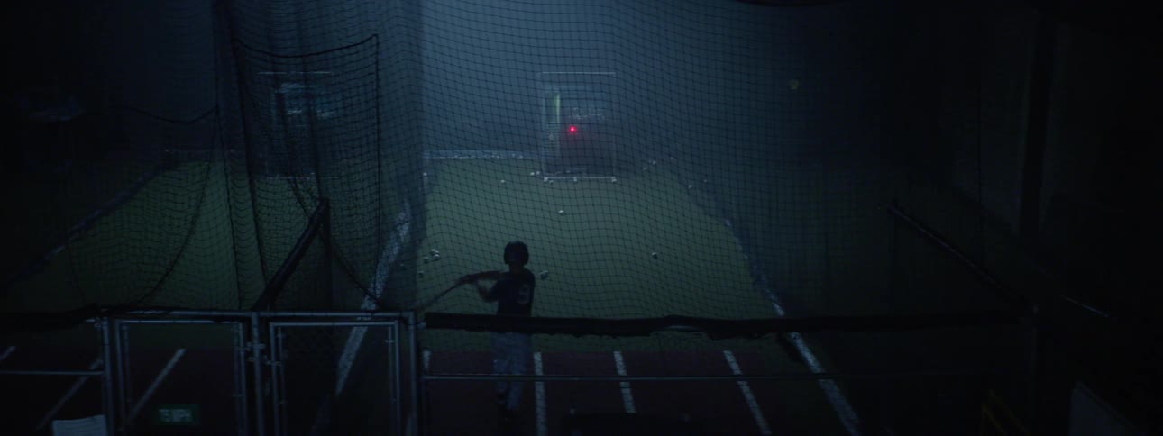 Baseball player takes swings at a baseball from a pitching machine in a batting cage
