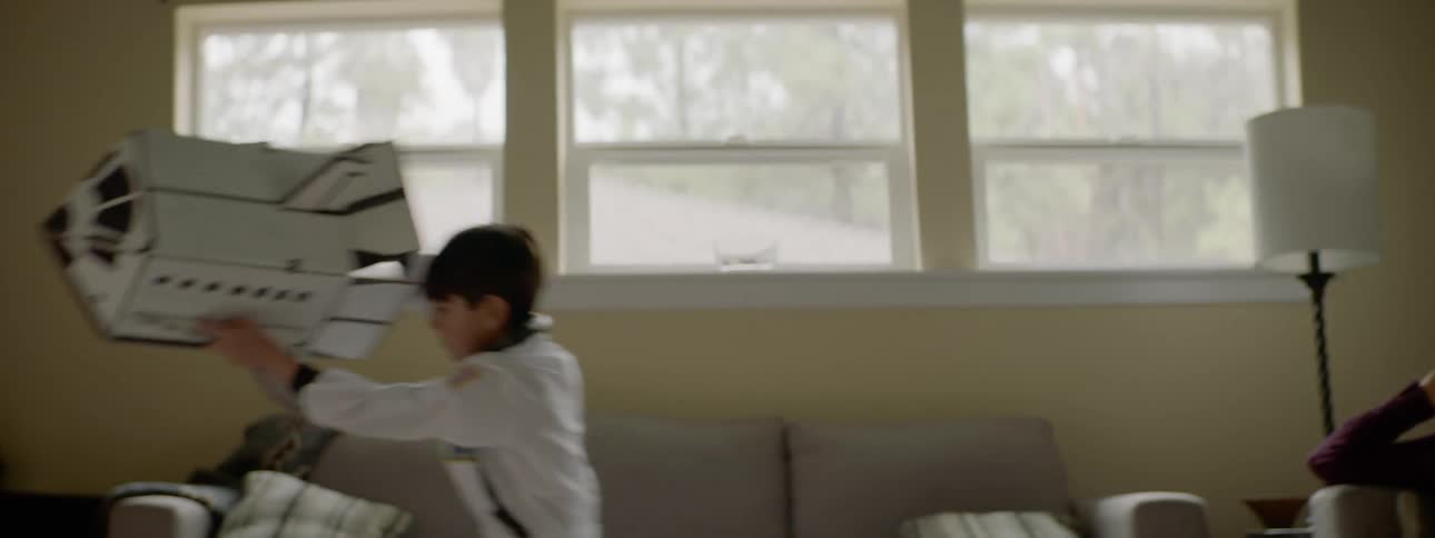 Woman talks on phone while boy runs around living room with space shuttle model