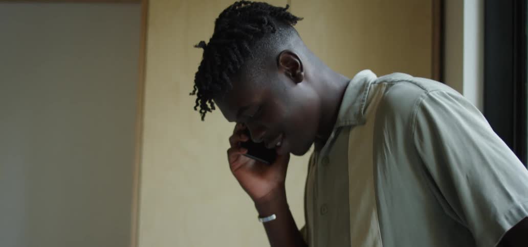 A young black male talks on a cell phone in his room