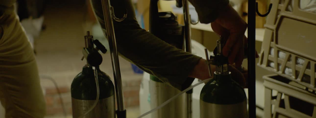 A white man puts a clear tube on an oxygen tank