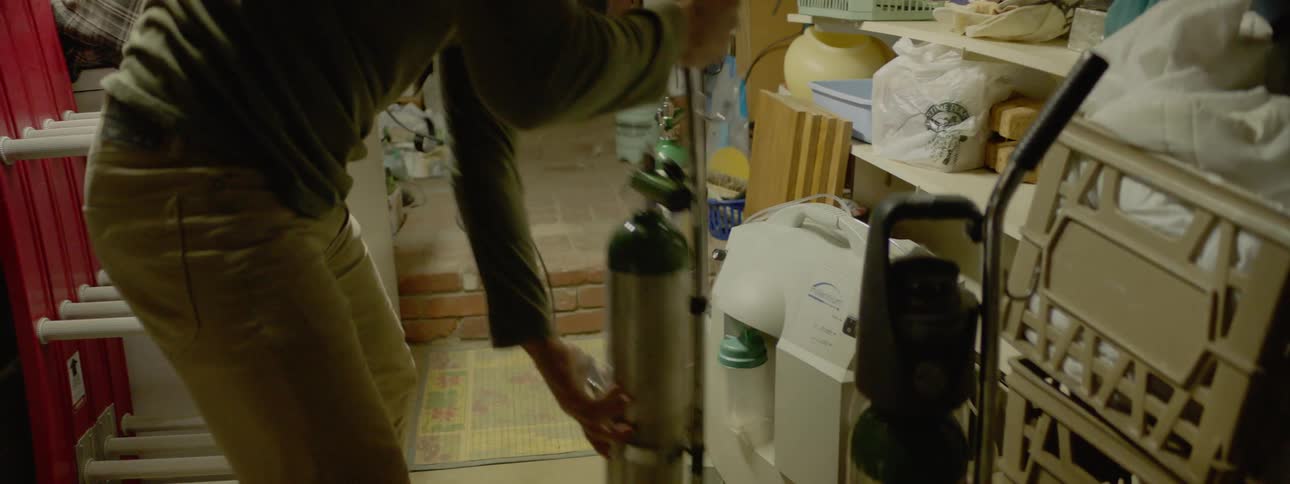 A white man moves oxygen tanks in a cramped storage space