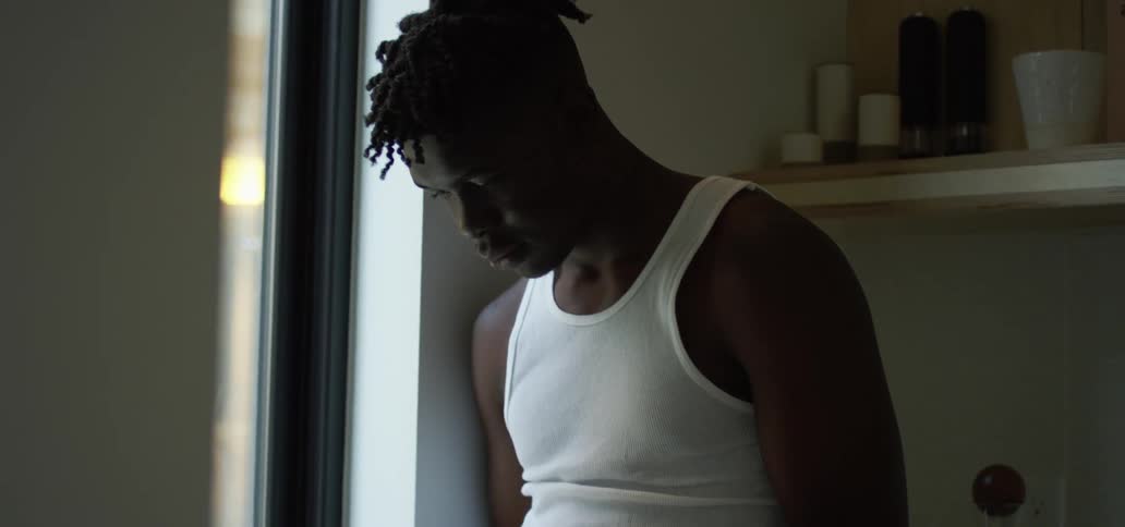 A young black man leans against a counter at home and scrolls on his cell phone