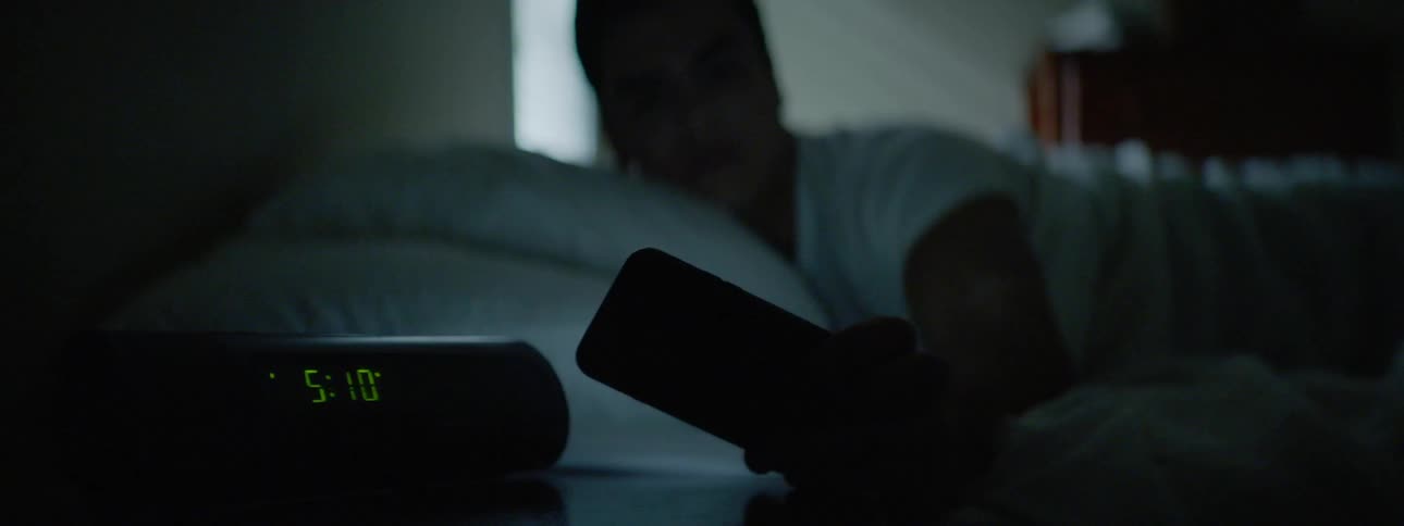 A man lying in bed wakes up and grabs his cell phone