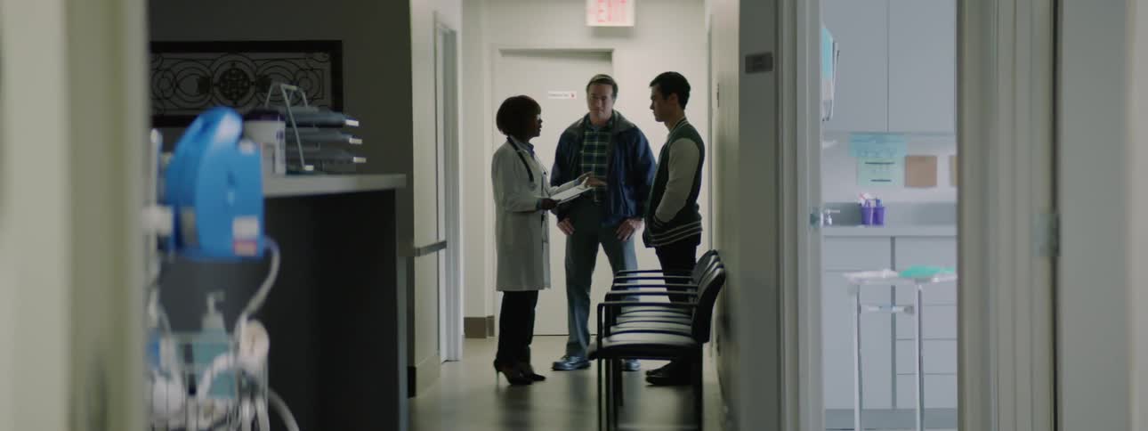 Doctor in white coat talks to father and son in clinic near examination room