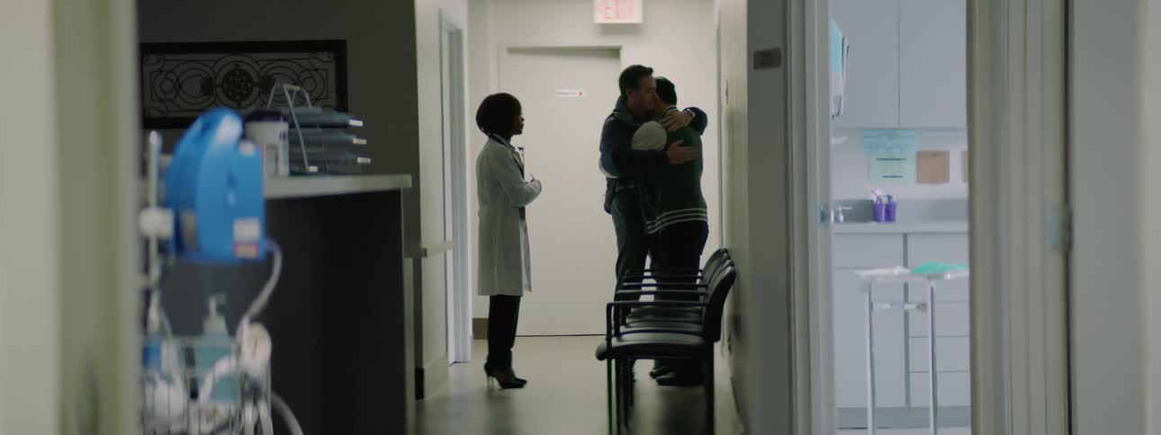 A doctor steps back to give a dad a chance to hug and comfort his son in a hospital hallway
