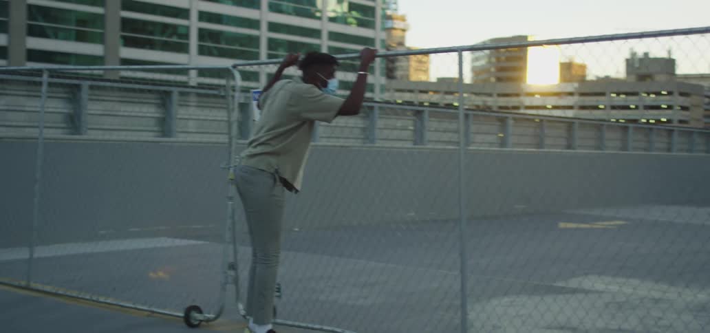 A black man wearing a mask looks over a fence