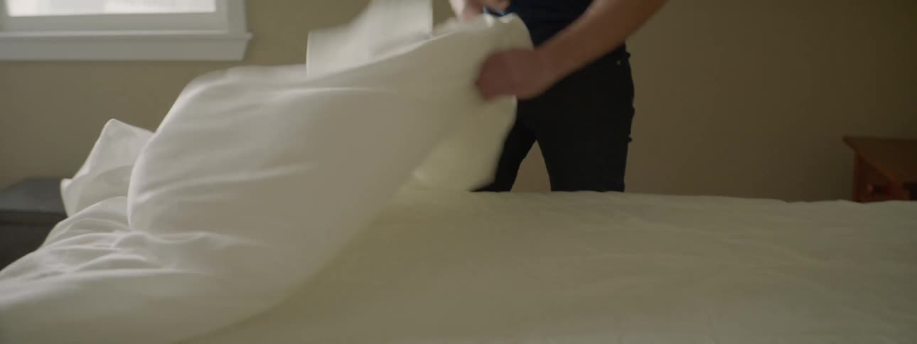 Young man takes the bed sheets out of a matress in a bedroom
