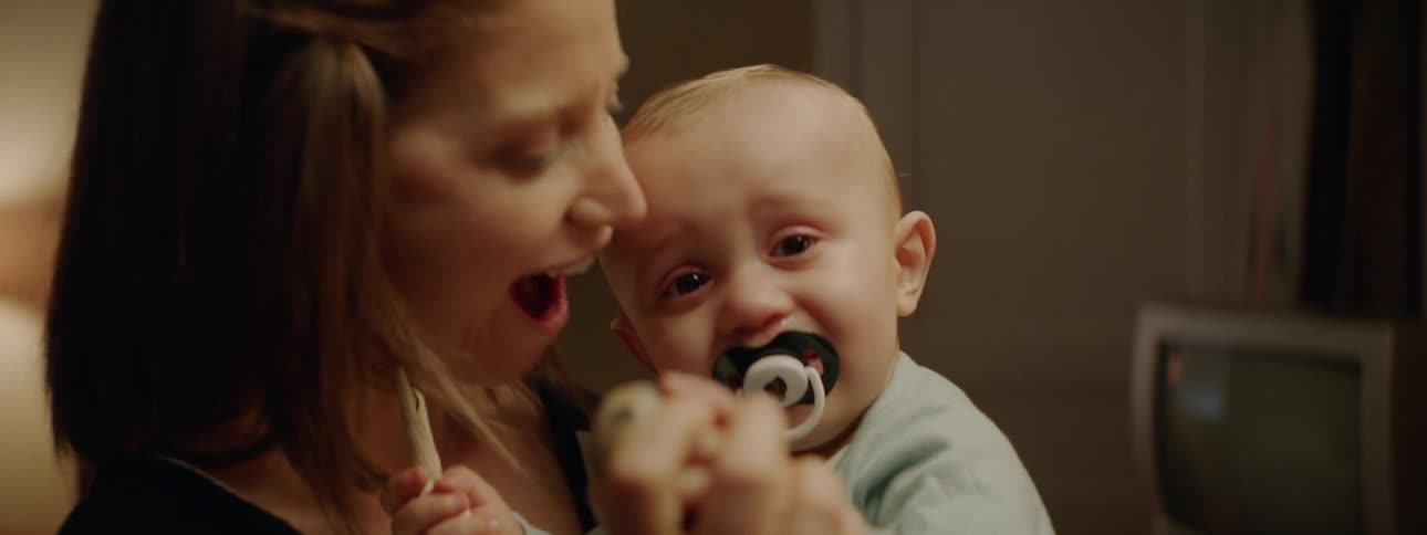A mother holds and cuddles her baby in a living room