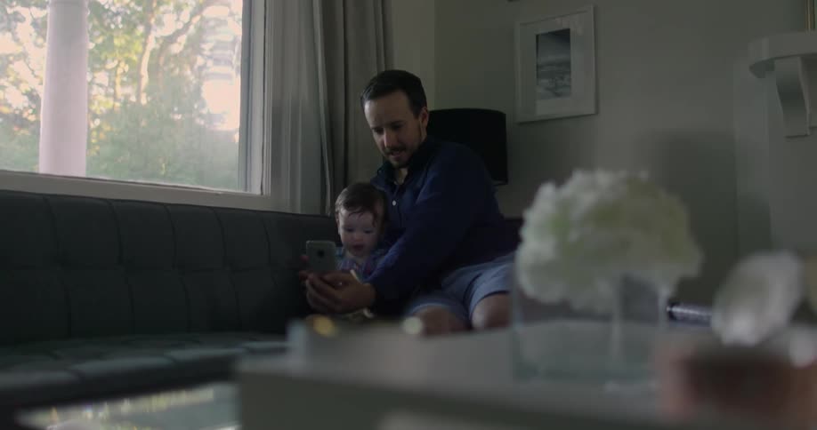 A father sits with his son and takes selfies on his cell phone inside their home