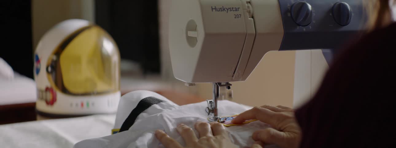 A woman in her home sews a badge on a shirt