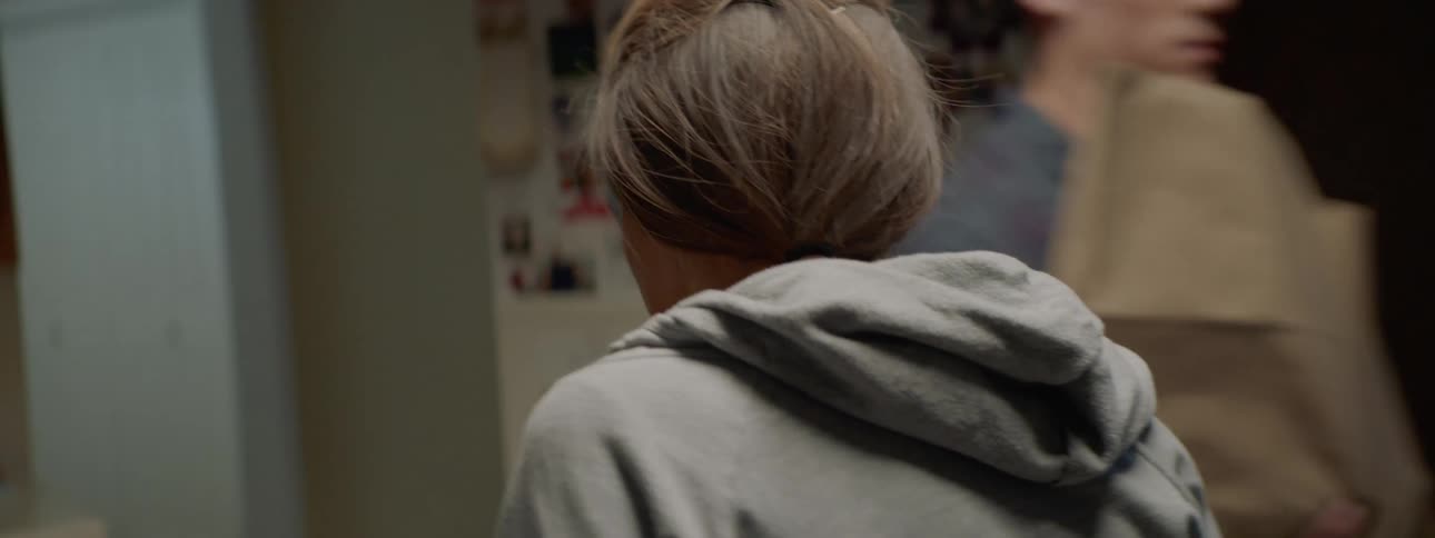 A young man walks in to a kitchen with bags of groceries and storms past his mother