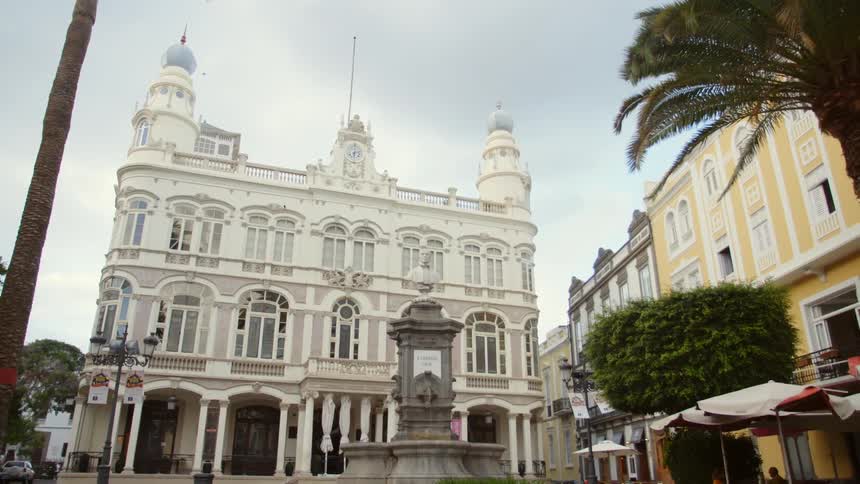 Wind blows the palm tree fronds in the square near a monument and ornate buildings
