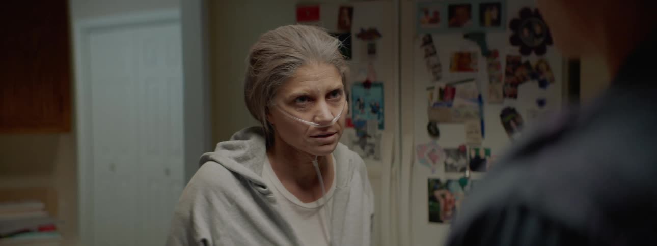 An elderly woman using an oxygen tank speaks to her son in the kitchen