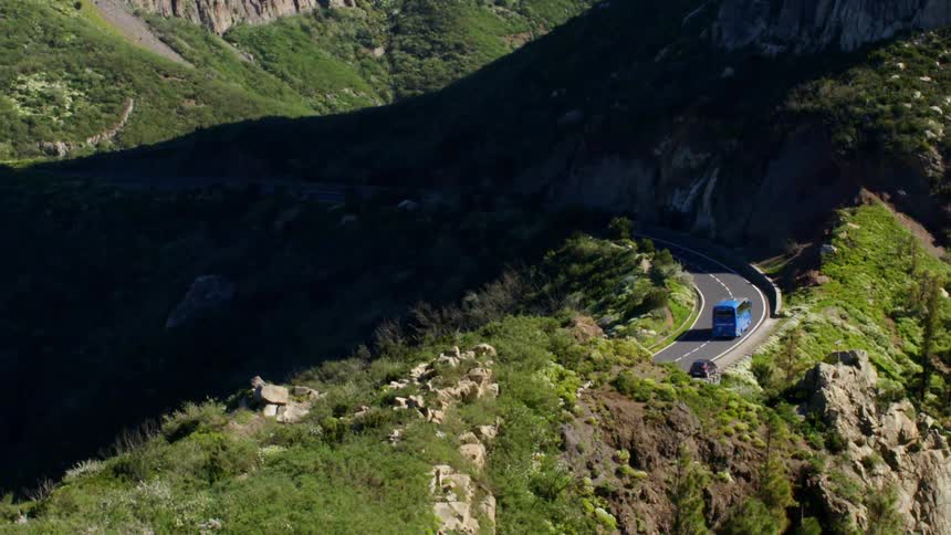 A blue bus traveling along a curve on a mountain road