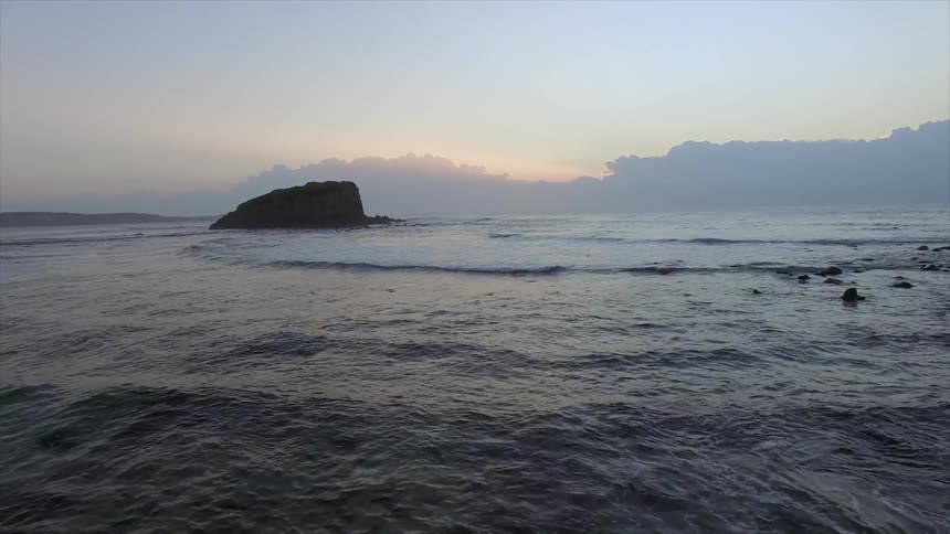 A large rock in the middle of a calm sea during sunset
