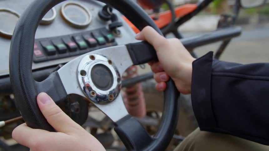 A young man sits in a farm vehicle outdoors while holding the steering wheel with both hands