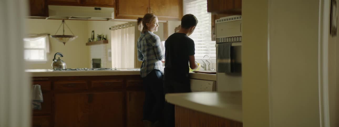 A mother and her son do dishes together in the kitchen