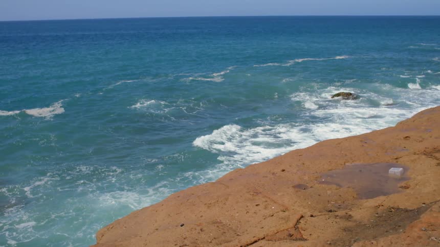 The soft waves of the blue ocean off a stone coastline on a sunny day