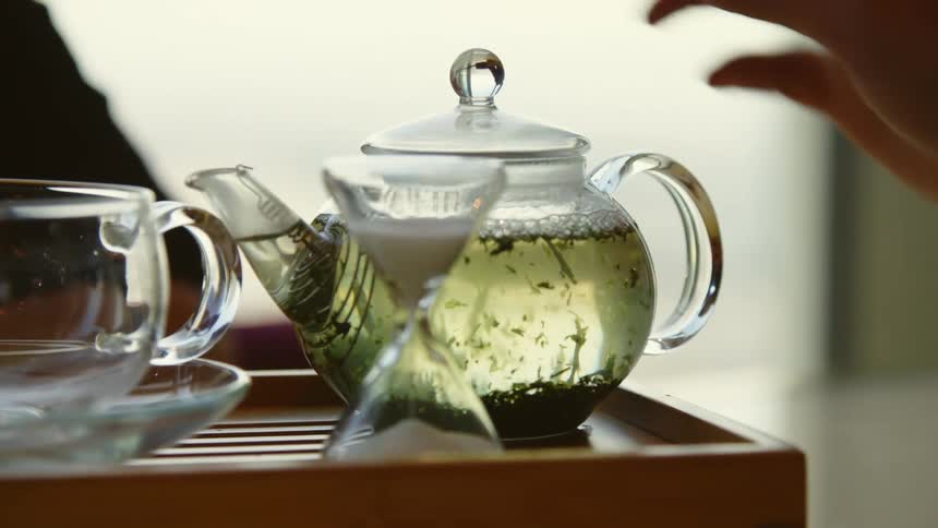 Green tea brewing in a glass kettle on wood tray