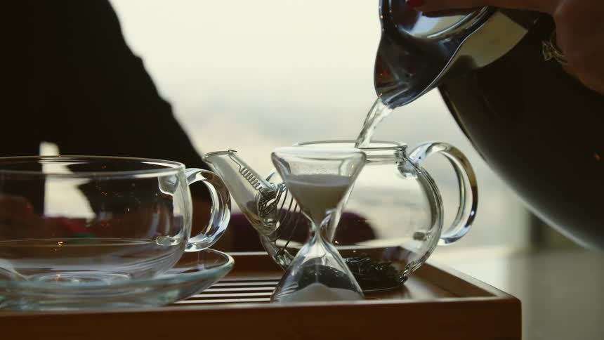 A person is pouring water into a glass tea pitcher