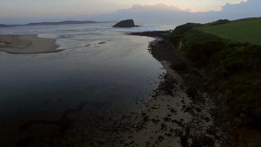 Aerial view of a rocky shoreline and lush cliffs during a cloudy sunset