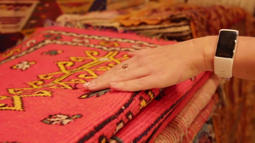 A white woman runs her hand over a pile of rugs