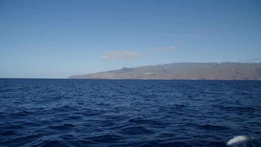 Small waves crash in the ocean far from a promontory