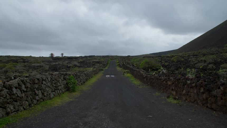 A road lined with stone walls leading through a rocky countryside