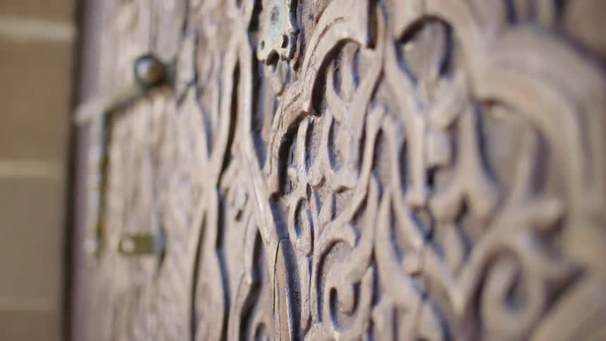 Ornately carved door in brick wall has bronze hinges