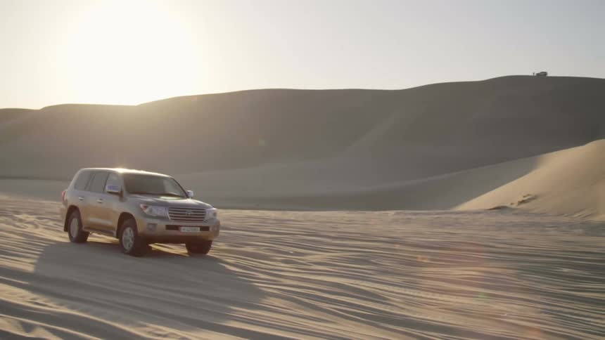 All terrain vehicle driving on the sand of a desert near dunes at sunset
