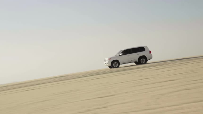 A white car with four wheel drive drives downhill in desert