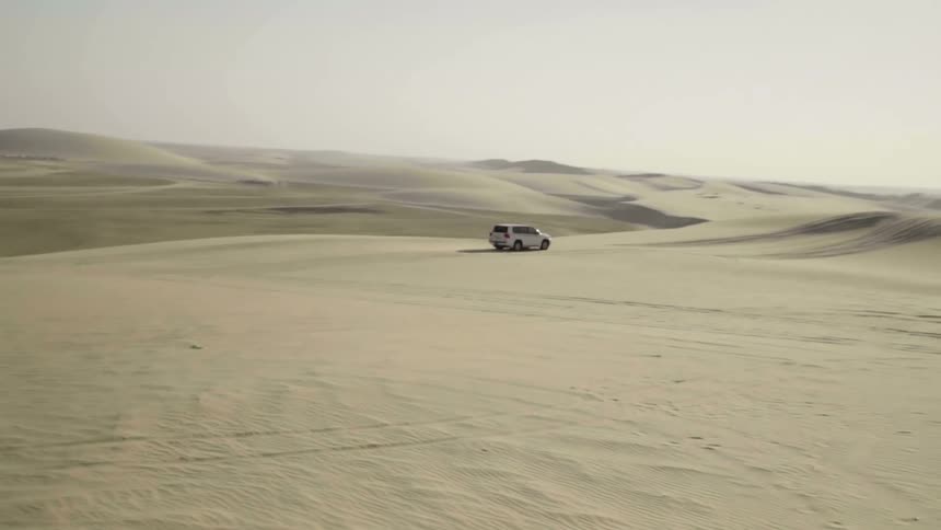Suv drives across desert stretching toward the mountains on the horizon