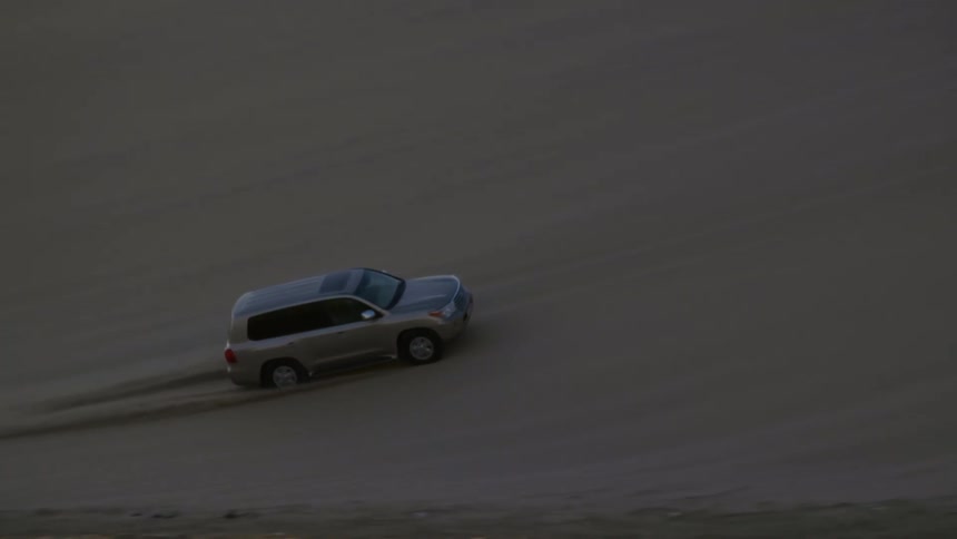A sport utility vehicle drives up the slope of a sand dune in the desert