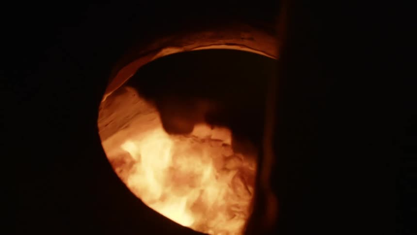Person places flat bread inside an open fire earthen oven