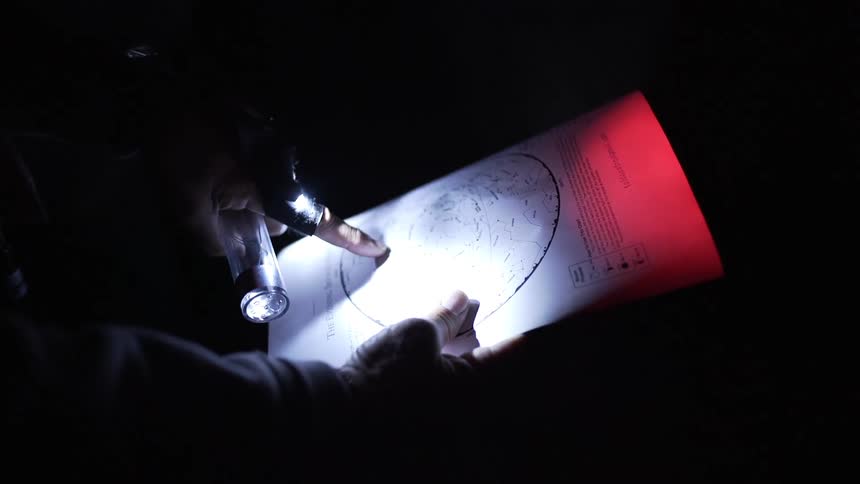 A white man looks over a map lit up by a flashlight