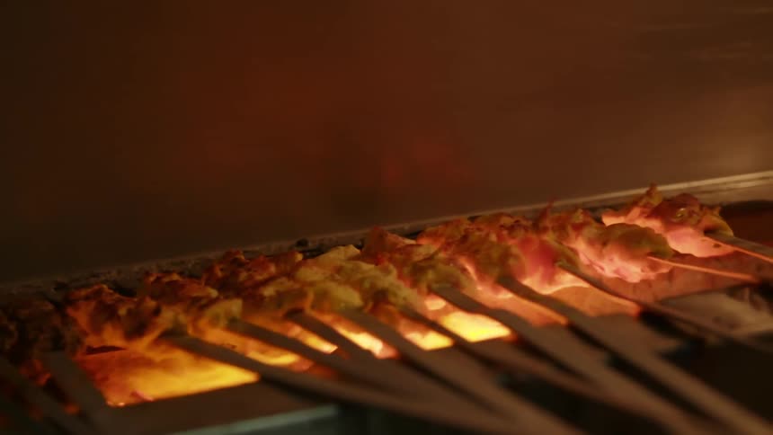 A persons hand putting shish kebabs on a grill