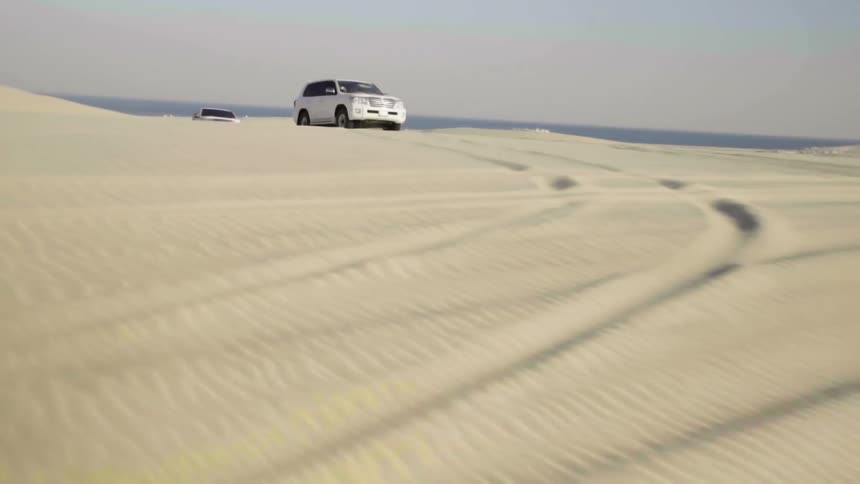 Convoy of cars driving across sand dunes in the desert
