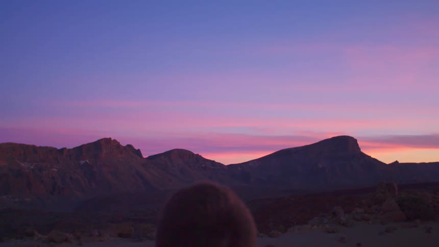 Man with a coat stands and watches the distant mountains against the red sky