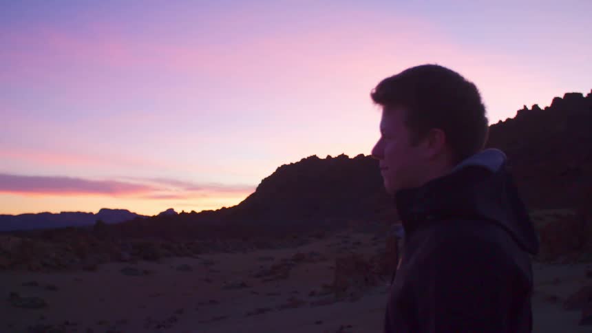 Man stands near the mountains under a red sky at dusk