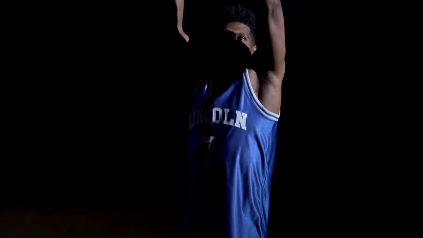 Young basketball player shoots a basketball in a dimly lit room
