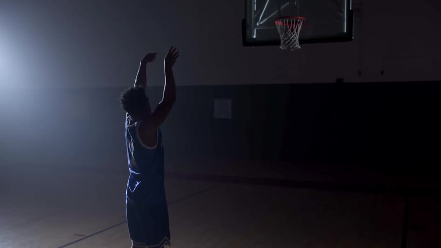 A young man practices shooting basketball free throws in a gymnasium
