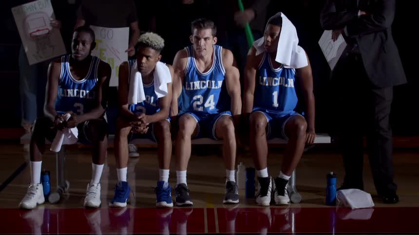 Four team members wearing jerseys sit on the bench in front of the fans
