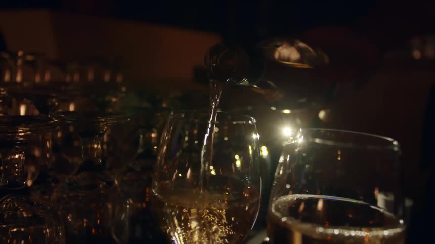 A person pours wine in to glasses at a bar