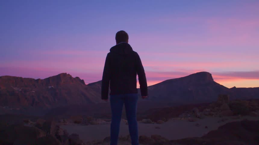 A man stands with his fists tightly clenched as he looks over a canyon