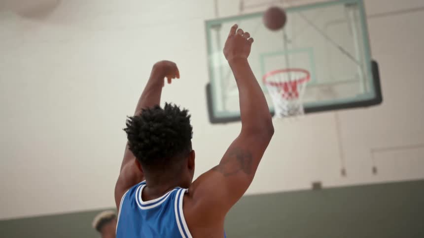 A man throws a basketball toward the hoop in a basketball game and makes the shot