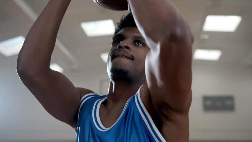 A man in a basketball uniform shooting a basketball in an indoor gym